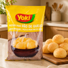 A bag of Yoki Cheese Bread Mix (Mistura para Pão de Queijo) on a kitchen counter next to fresh golden-brown bread rolls.